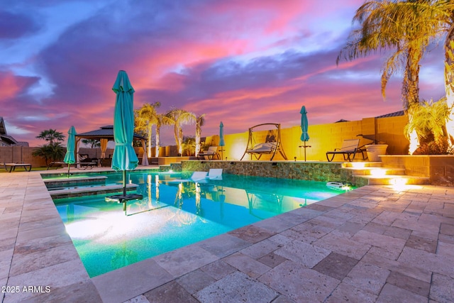 pool at dusk with a gazebo, pool water feature, an in ground hot tub, and a patio area