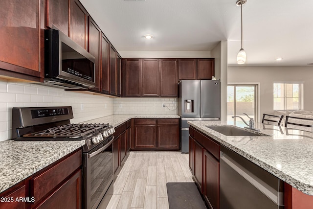 kitchen featuring a sink, light stone counters, decorative light fixtures, stainless steel appliances, and decorative backsplash