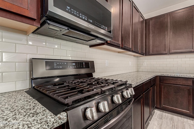 kitchen featuring dark brown cabinetry, decorative backsplash, appliances with stainless steel finishes, and light stone countertops