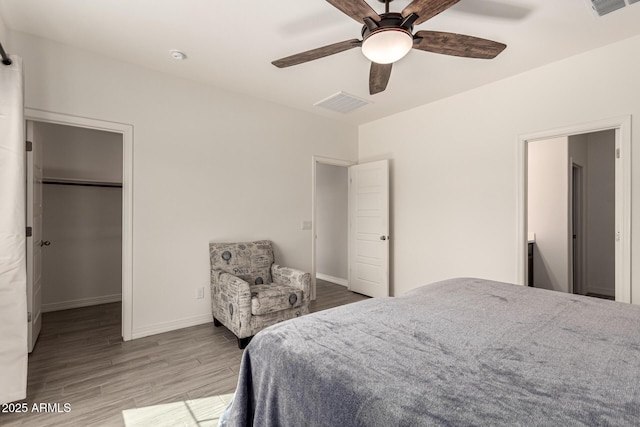 bedroom with visible vents, a walk in closet, wood finished floors, baseboards, and ceiling fan