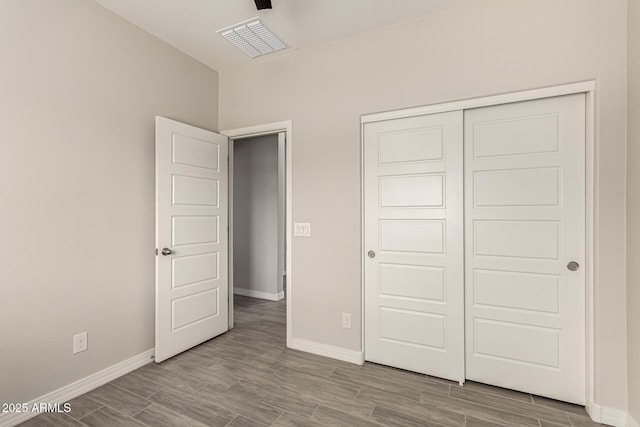 unfurnished bedroom featuring wood finished floors, visible vents, a closet, and baseboards