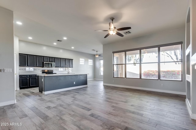 kitchen with stainless steel appliances, plenty of natural light, a kitchen island with sink, and light wood-type flooring