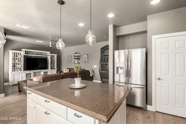 kitchen with a center island, stainless steel refrigerator with ice dispenser, light wood finished floors, visible vents, and white cabinetry