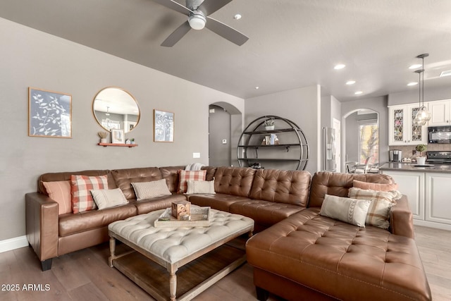 living room featuring arched walkways, light wood finished floors, a ceiling fan, and recessed lighting