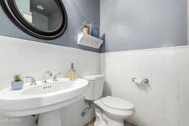 bathroom featuring a wainscoted wall, a sink, toilet, and tile walls