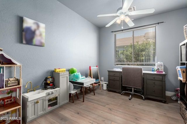 office space featuring light wood finished floors, baseboards, a ceiling fan, and a sink