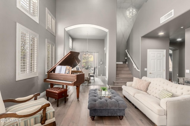 living area featuring a notable chandelier, wood-type flooring, visible vents, stairway, and a high ceiling