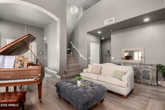 living area with arched walkways, visible vents, stairway, a towering ceiling, and wood finished floors