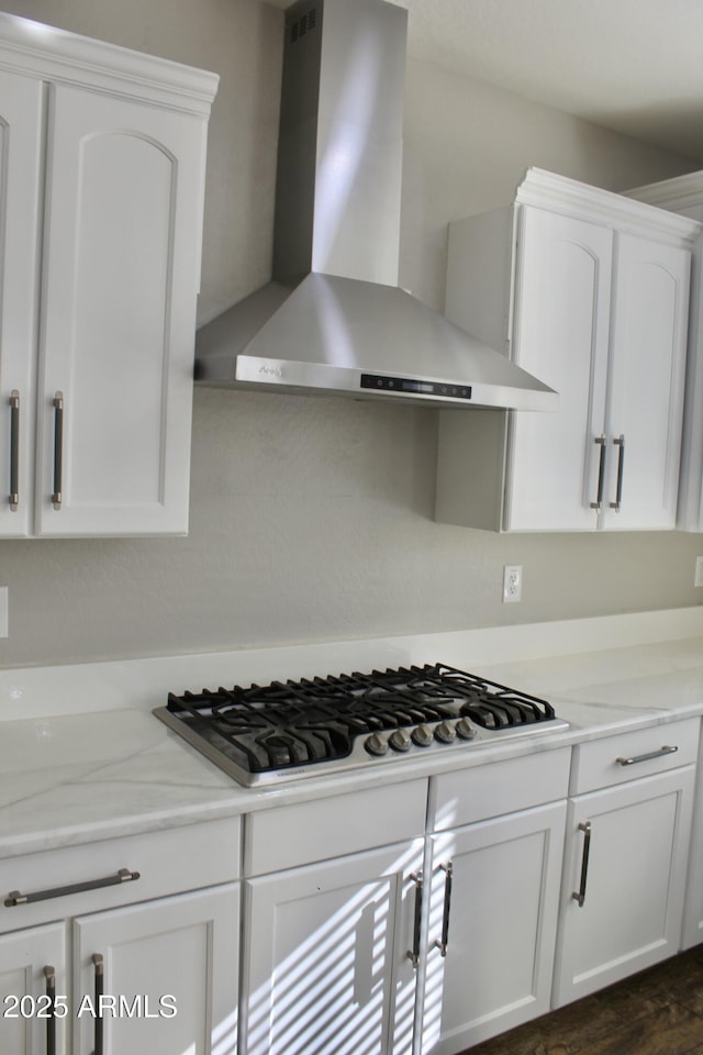 kitchen featuring white cabinets, gas stovetop, light stone countertops, and wall chimney range hood