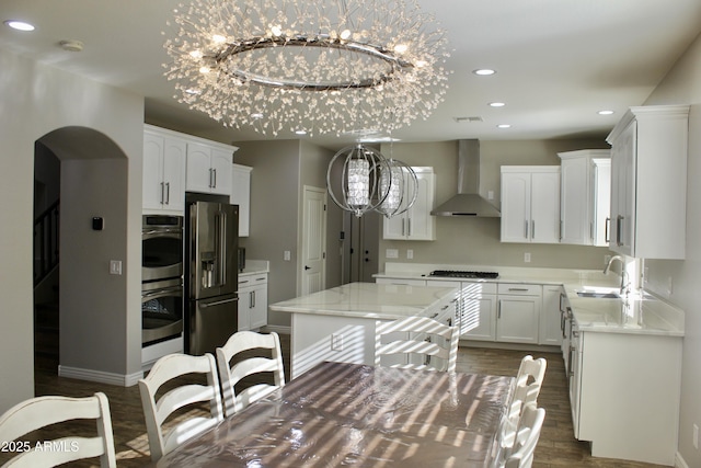 kitchen with a notable chandelier, wall chimney exhaust hood, white cabinets, and appliances with stainless steel finishes