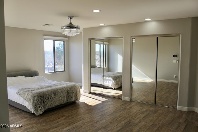 bedroom with a chandelier, dark wood-type flooring, and multiple closets