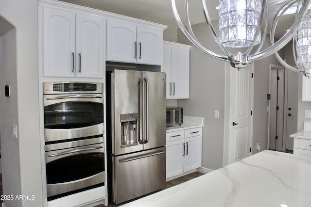 kitchen featuring white cabinets, light stone counters, appliances with stainless steel finishes, and an inviting chandelier