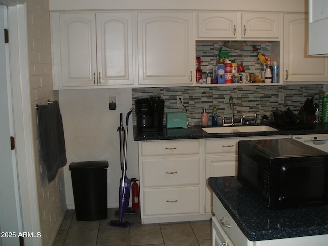 kitchen with light tile patterned floors, decorative backsplash, white cabinetry, a sink, and black microwave