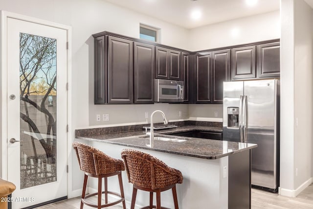 kitchen with stainless steel appliances, sink, dark stone countertops, and kitchen peninsula