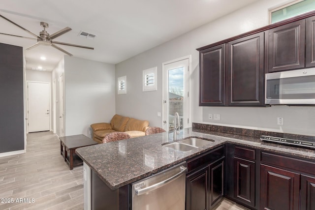 kitchen with sink, stainless steel appliances, kitchen peninsula, dark stone counters, and light wood-type flooring