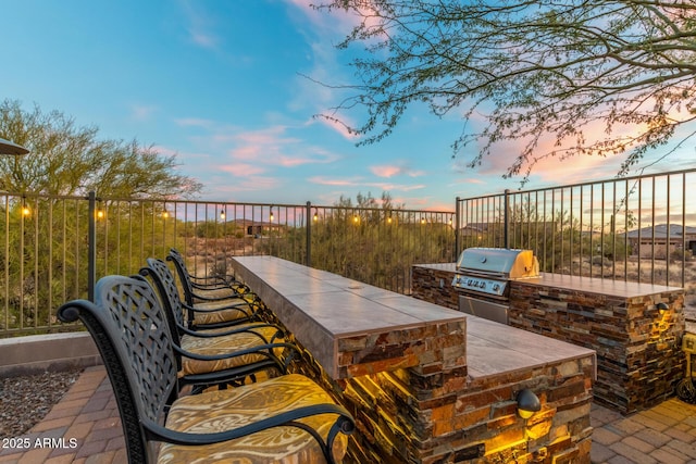 patio terrace at dusk with area for grilling, grilling area, and exterior bar