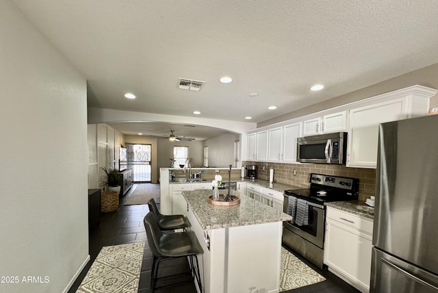 kitchen featuring a breakfast bar area, stainless steel appliances, a center island, white cabinets, and kitchen peninsula