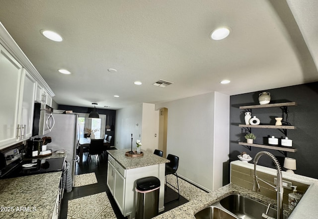 kitchen with light stone countertops, a kitchen island, sink, and white cabinets