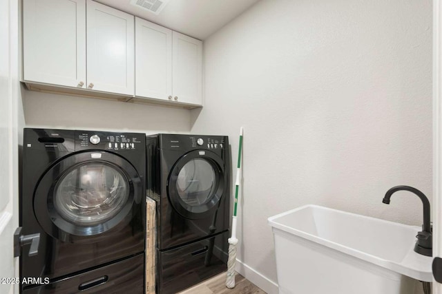 laundry area with wood finished floors, visible vents, cabinet space, a sink, and washer and dryer