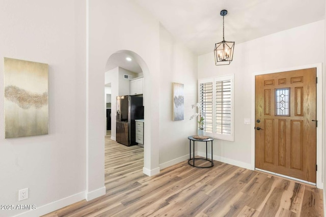 entrance foyer featuring visible vents, baseboards, arched walkways, and light wood-style flooring