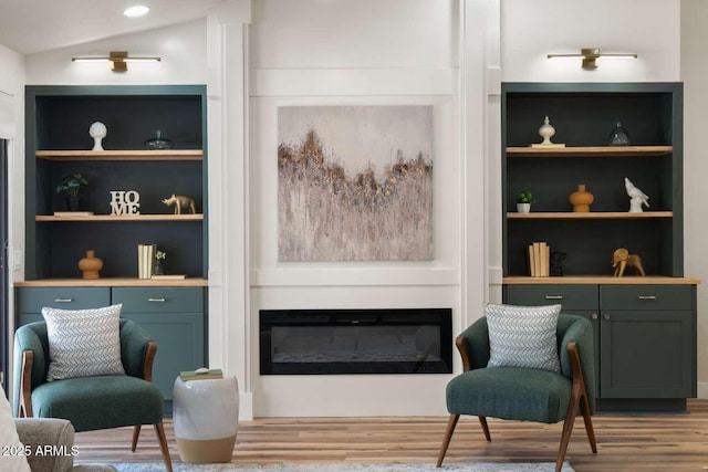 living area featuring a glass covered fireplace, lofted ceiling, built in shelves, and wood finished floors