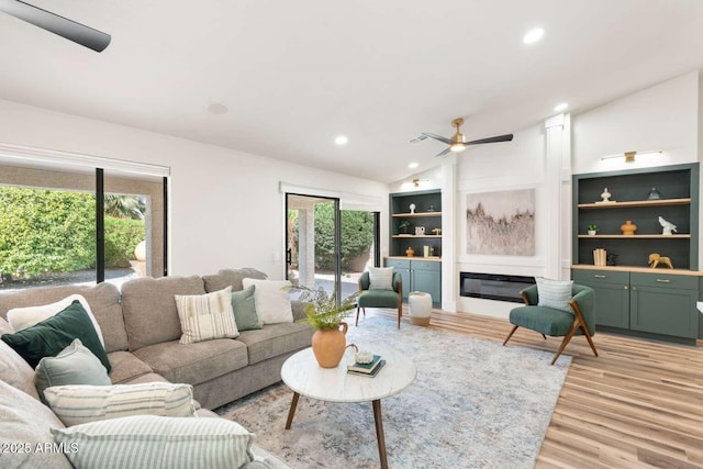 living area with a wealth of natural light, lofted ceiling, a glass covered fireplace, and light wood finished floors