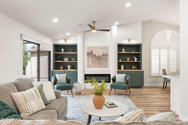 living area with visible vents, light wood-style flooring, recessed lighting, vaulted ceiling, and a glass covered fireplace