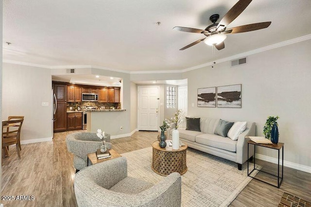 living room featuring baseboards, light wood-style flooring, visible vents, and crown molding