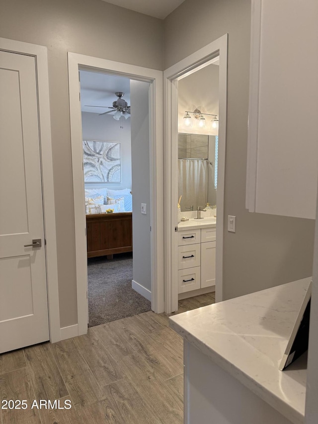 interior space with vanity, a ceiling fan, baseboards, wood finished floors, and ensuite bathroom