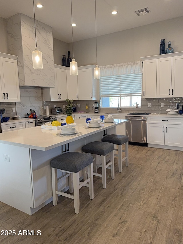 kitchen featuring stainless steel appliances, decorative backsplash, a breakfast bar, visible vents, and white cabinetry