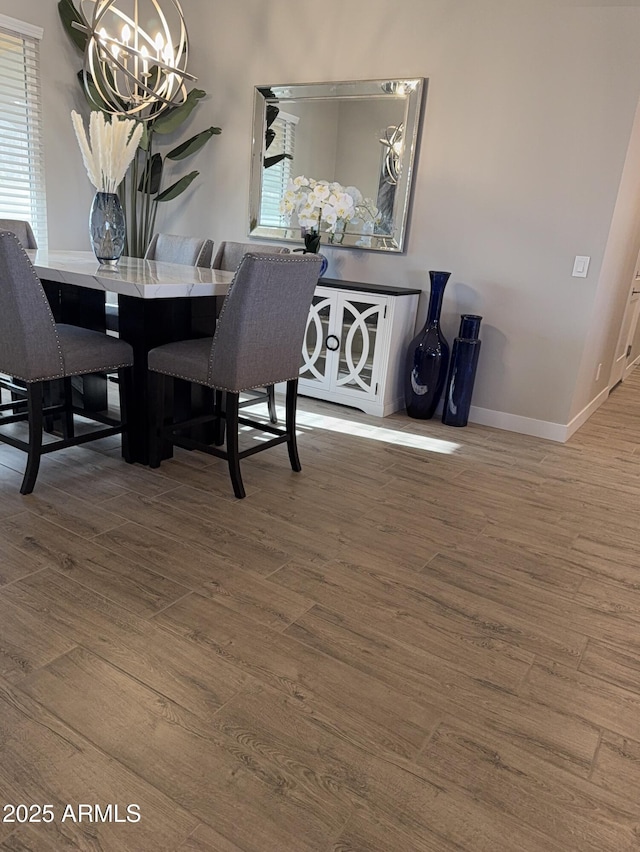 dining area featuring wood finished floors, a healthy amount of sunlight, a notable chandelier, and baseboards