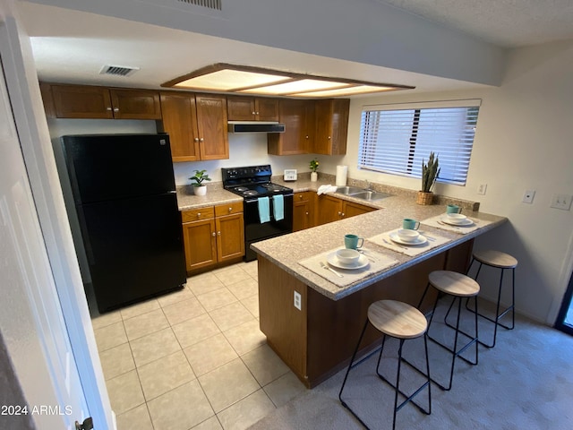 kitchen featuring black appliances, sink, light tile patterned floors, a kitchen bar, and kitchen peninsula