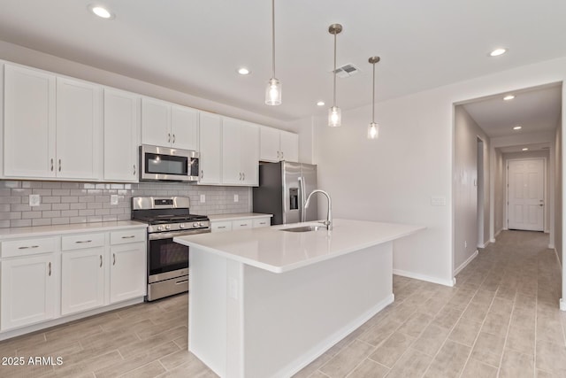 kitchen featuring sink, hanging light fixtures, appliances with stainless steel finishes, an island with sink, and white cabinets