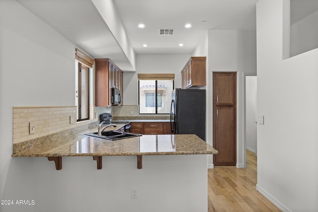 kitchen with visible vents, a breakfast bar, a peninsula, black appliances, and a sink