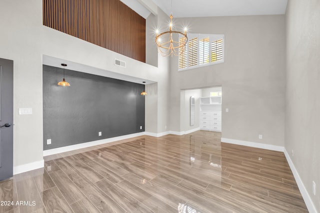 unfurnished living room with hardwood / wood-style flooring, a towering ceiling, and an inviting chandelier