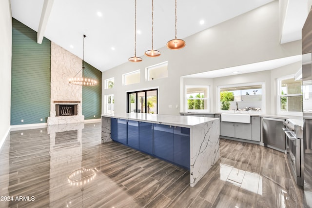 kitchen featuring sink, decorative light fixtures, high vaulted ceiling, a stone fireplace, and a large island