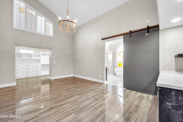 unfurnished living room featuring a barn door, wood-type flooring, a high ceiling, and an inviting chandelier