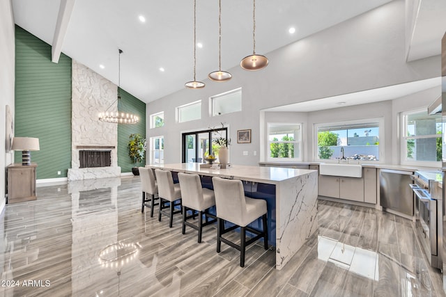 kitchen featuring light stone countertops, sink, high vaulted ceiling, a stone fireplace, and a large island