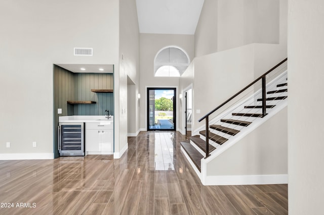 foyer entrance featuring hardwood / wood-style flooring, high vaulted ceiling, wet bar, and beverage cooler