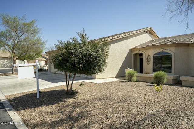 view of side of home with a garage, concrete driveway, a tile roof, and stucco siding