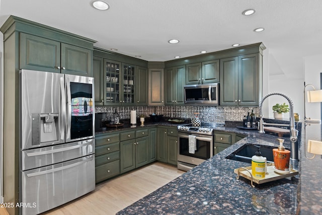 kitchen featuring backsplash, a sink, light wood-style flooring, dark stone countertops, and stainless steel appliances