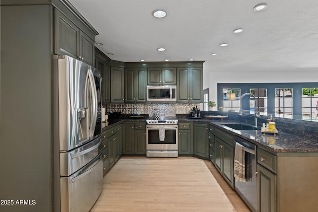 kitchen with decorative backsplash, a peninsula, stainless steel appliances, dark stone countertops, and a sink