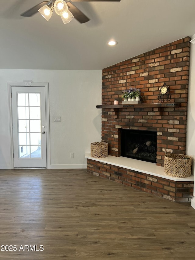 unfurnished living room with a brick fireplace, dark hardwood / wood-style floors, and ceiling fan