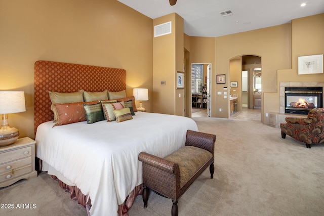 bedroom with visible vents, arched walkways, light colored carpet, and a fireplace