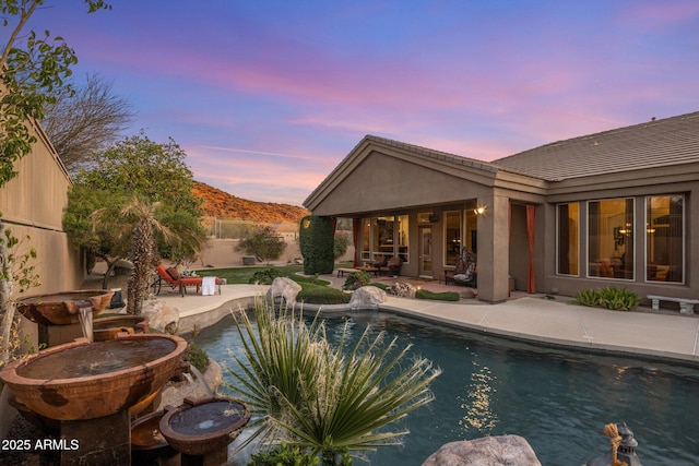 pool at dusk featuring a mountain view, a patio, a fenced in pool, and fence