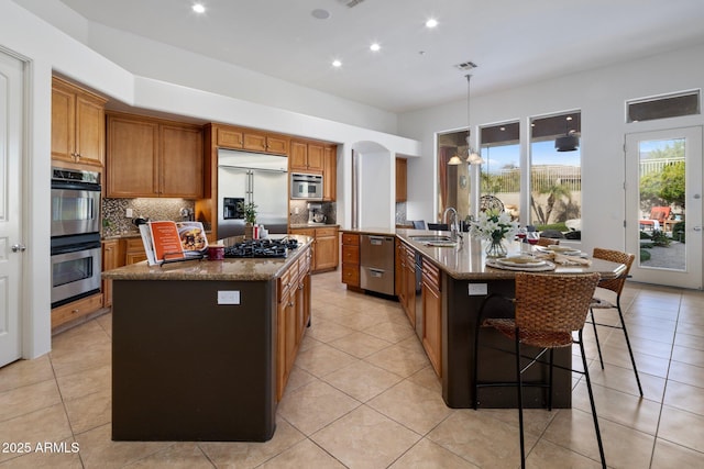kitchen with a sink, brown cabinetry, a spacious island, and stainless steel appliances
