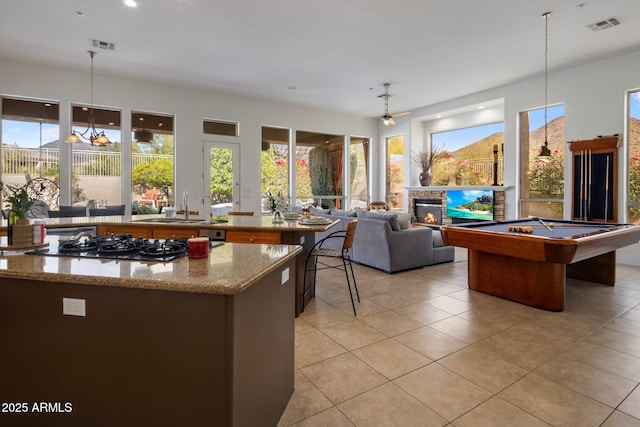 kitchen featuring visible vents, a sink, gas cooktop, a glass covered fireplace, and a center island