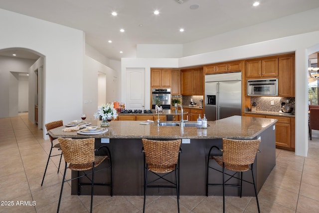 kitchen with a large island, a sink, stainless steel appliances, brown cabinetry, and decorative backsplash