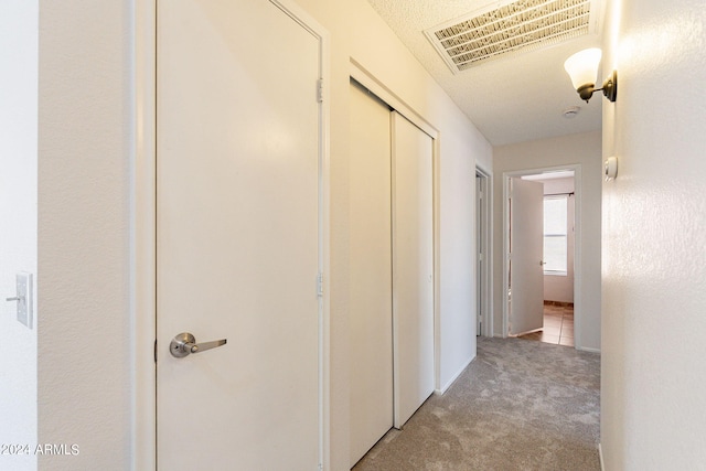 hall with light colored carpet and a textured ceiling