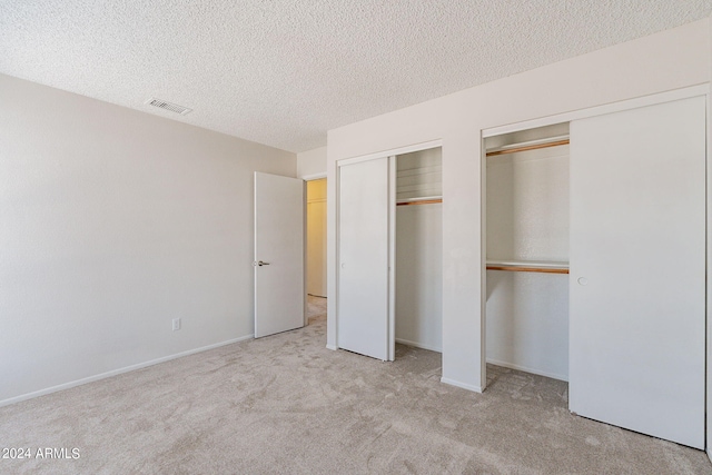 unfurnished bedroom featuring a textured ceiling, multiple closets, and light colored carpet